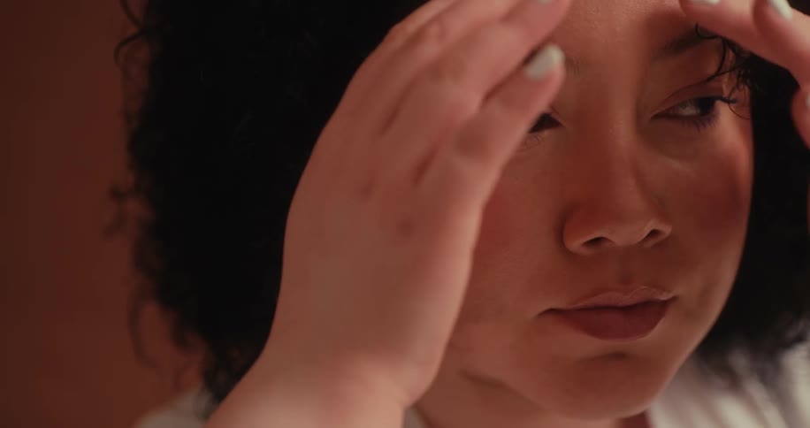 A young woman is using her fingers to fix her curly black hair