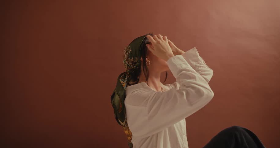 Woman posing while looking upward adjusts her hair