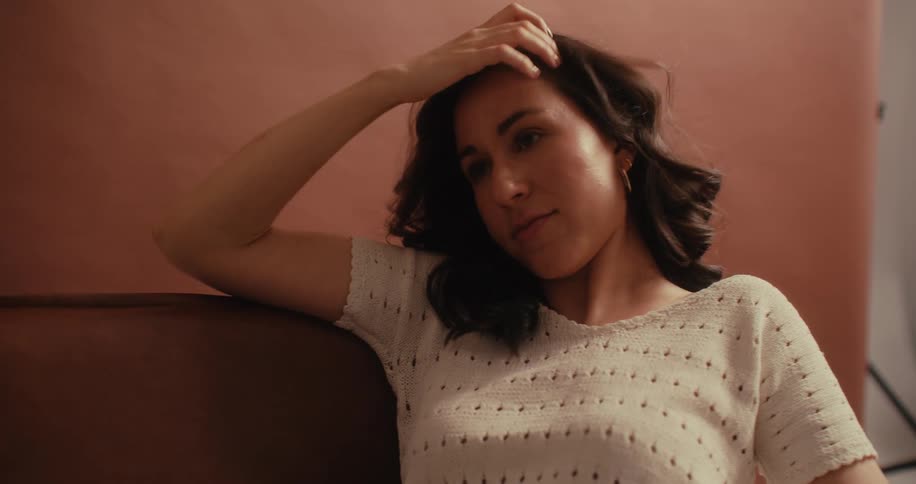A woman is fixing her hair as she sits on a couch by herself