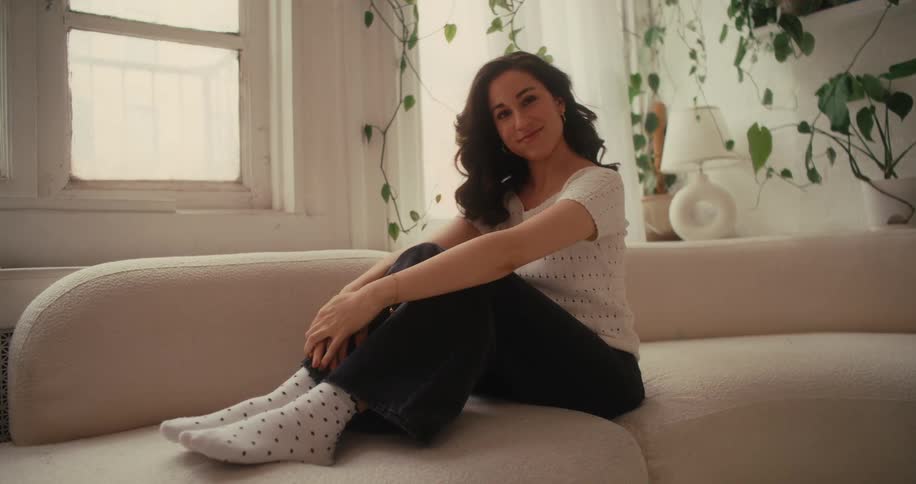A woman smiling sitting on a couch and flipping her hair