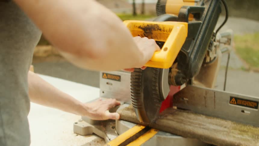 A woman is sawing wood planks outside