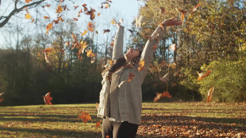 A young woman is playing outdoors in autumn leaves on a sunny day
