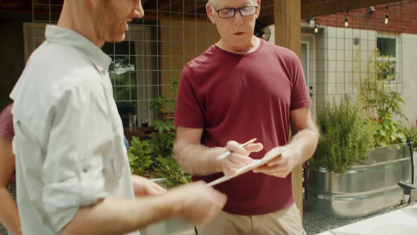 An older man explaining and showing a sheet of paper to a man and a woman