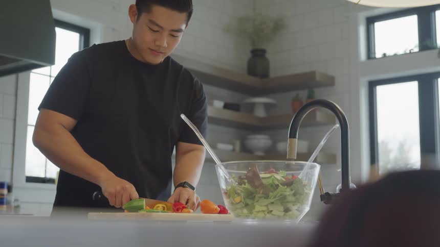 An asian man chops peppers while making a salad at home