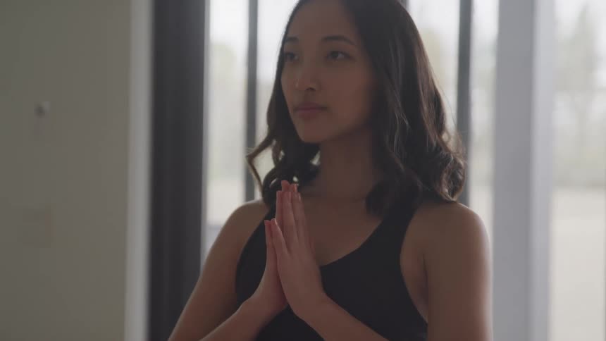 A woman with dark hair wearing a black top has her hands clasped in front of her