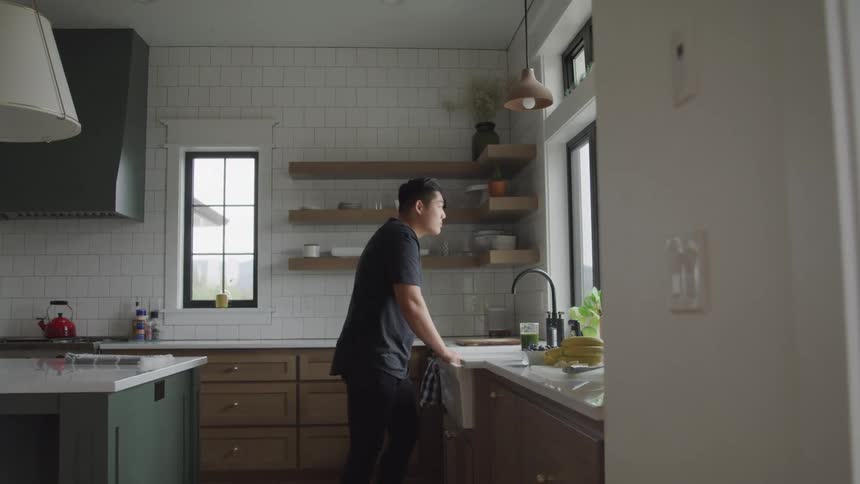 A young person leaning against a kitchen sink looking thoughtful