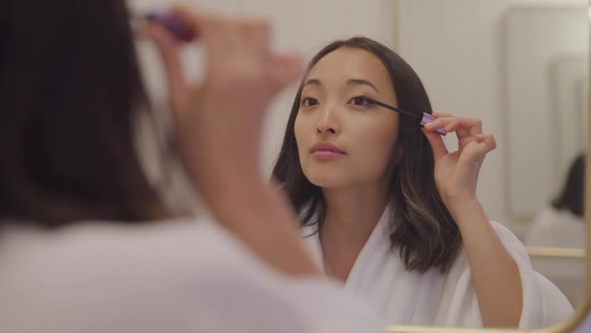 Woman in front of the mirror applying mascara to her eyelashes