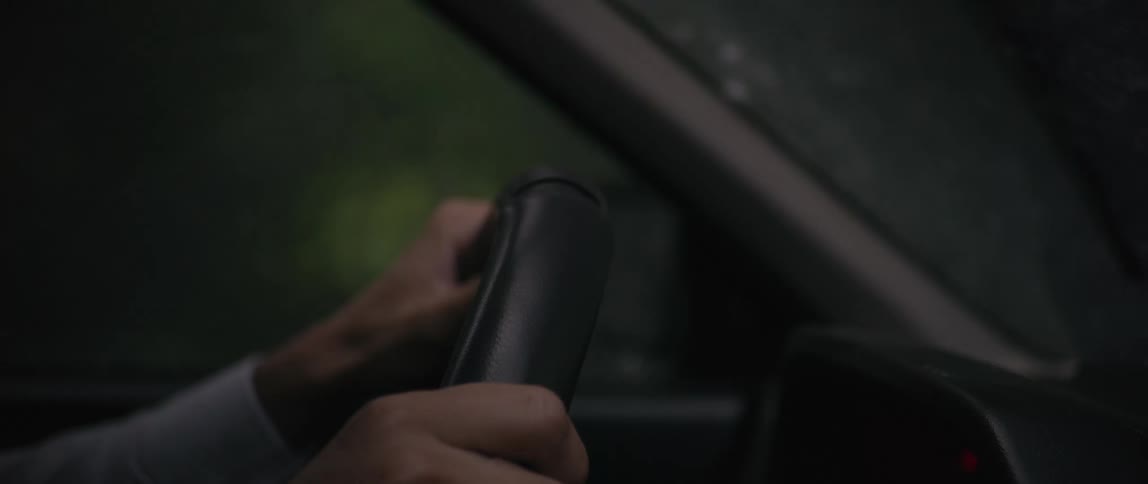 A person holds the steering wheel as they drive a car through a rain storm