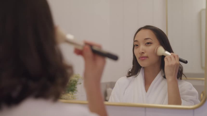 A woman in front of a mirror in the bathroom putting on makeup