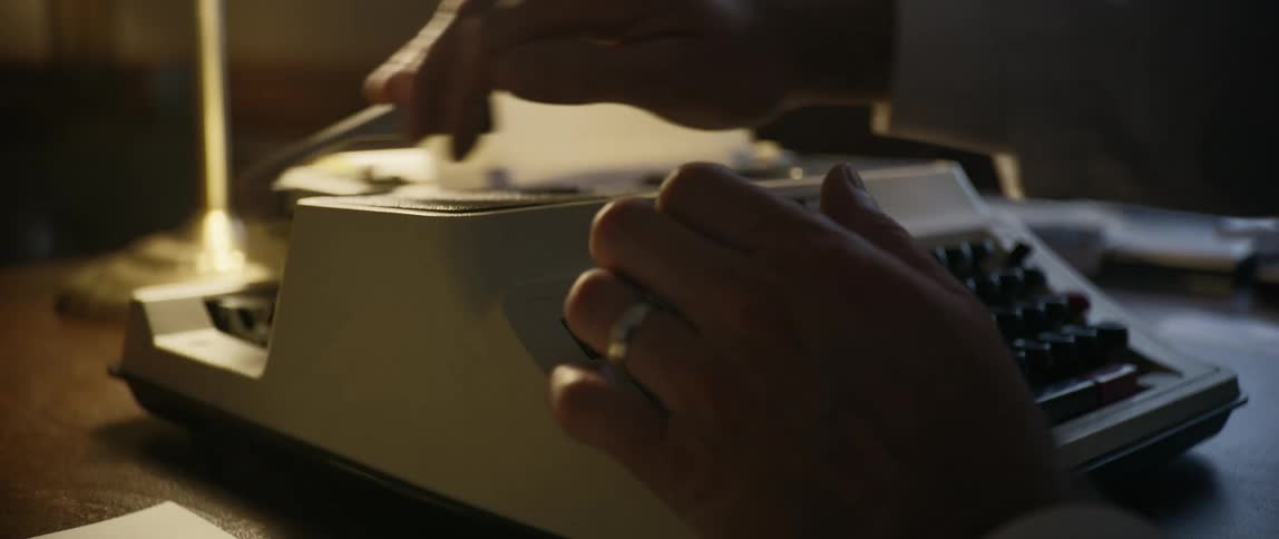 Person typing on an old school manual typewriter in a low lit office