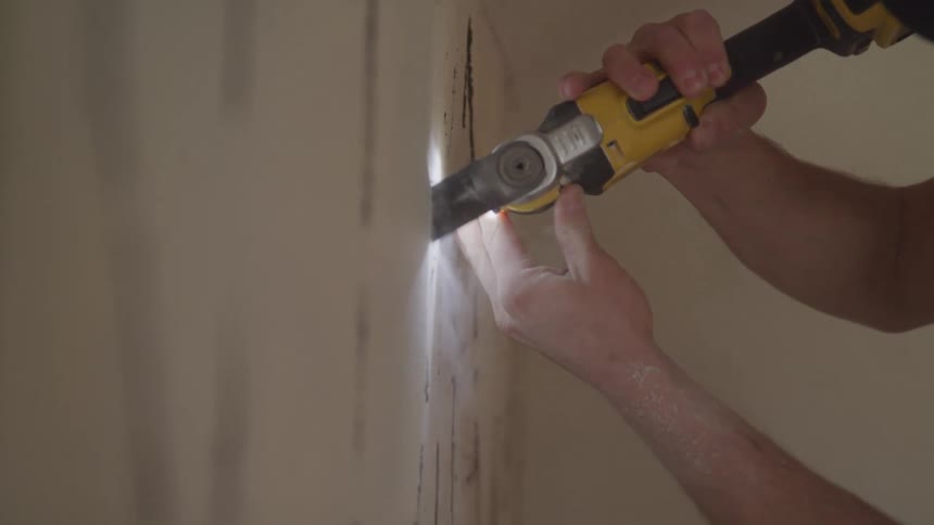 A man is using an oscillating tool to cut the wall
