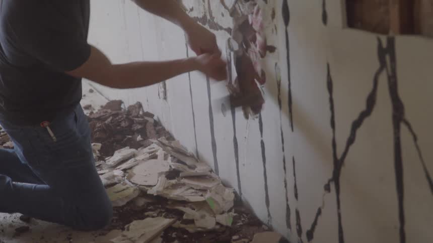 A construction worker is using a mallet to break up a wall in a building