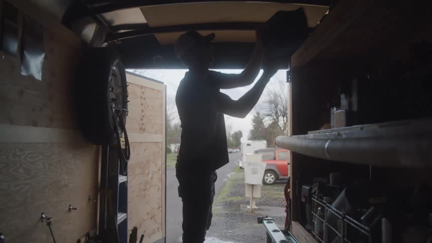 A man enters the back of a vehicle and grabs a tool bag