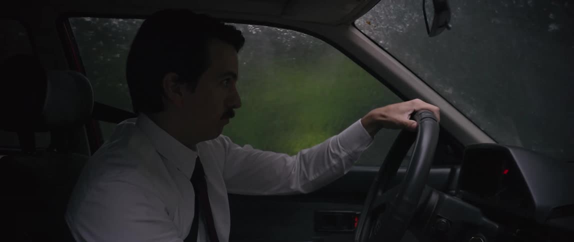 Man driving through torrentuous rain while wiping windshield and adjusting rearview mirror