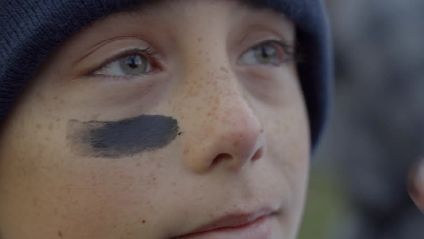 Person putting eye black on a boys face under his eyes