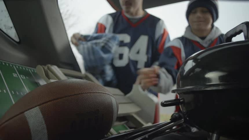 Man and child grabbing a blanket and football out of a vehicle