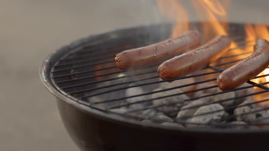 Person cooks hot dogs on grill