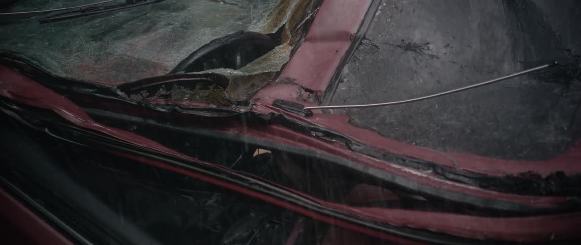 Rain pours down on a smashed red car