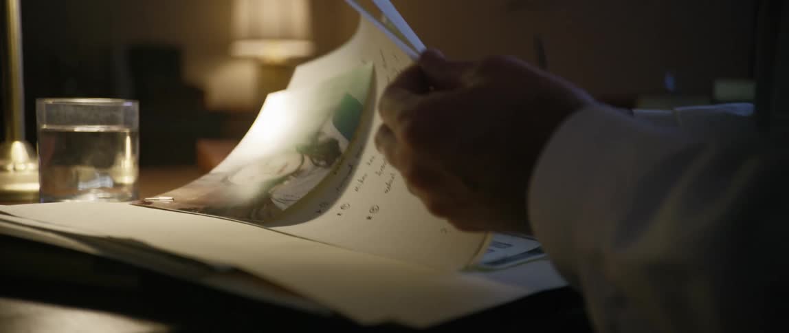 A man wearing a white dress shirt is sitting at a desk reading through a file