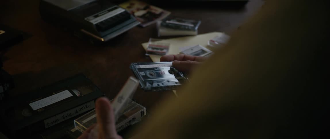 A person removes a cassette tape from a case and places both items on the desk in front of them