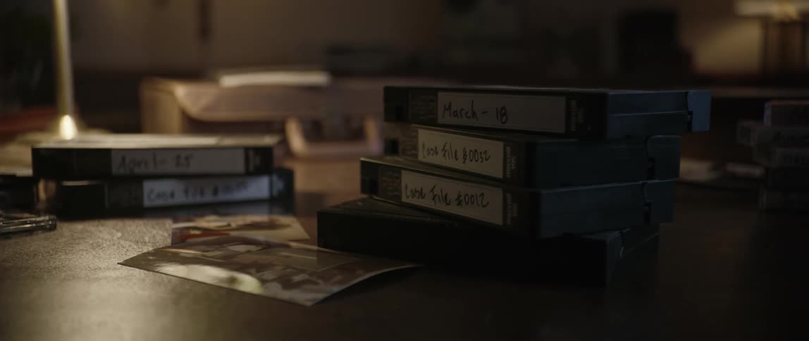 Stacks of vcr tapes and audio cassettes next to photos and a lit lamp o an office table