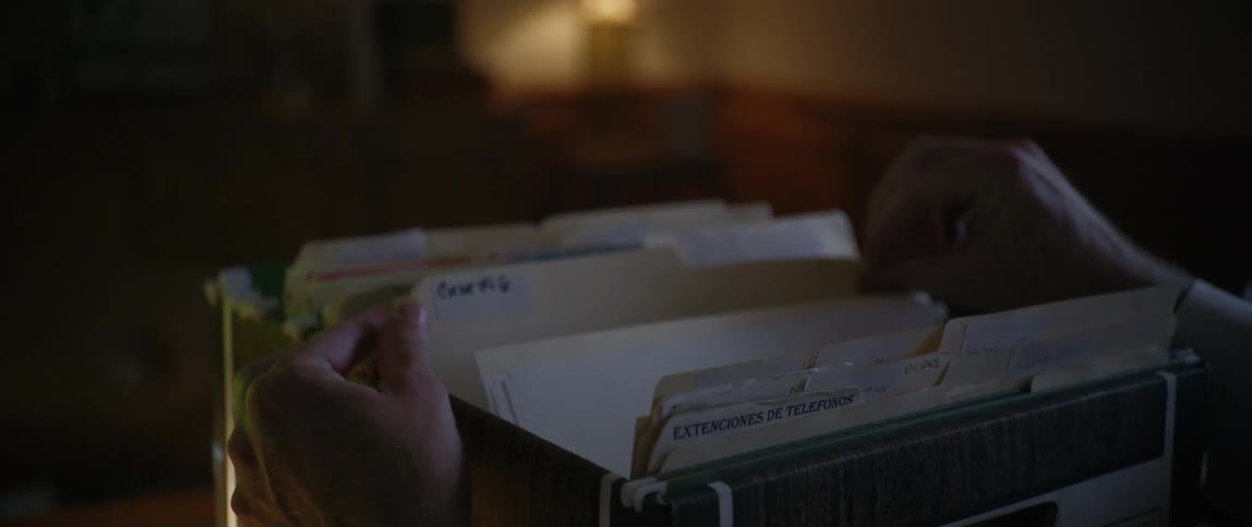 Man sitting in a low lit office searching through files from a cardboard file box