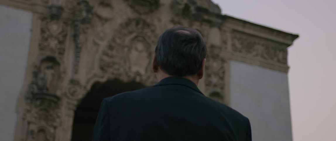 Man wearing a suit is admiring a church while the sun is setting