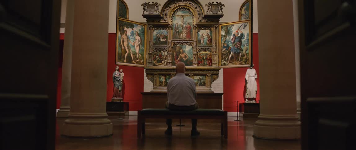 Person sitting on a church bench and looking at art paintings