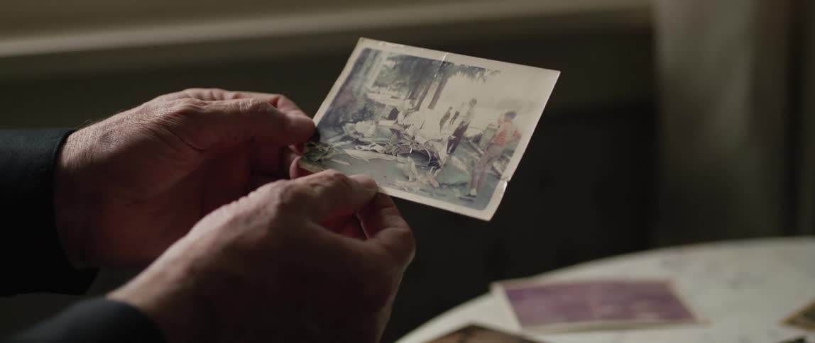 An elderly mans hands are holding a monochrome photograph of people outside