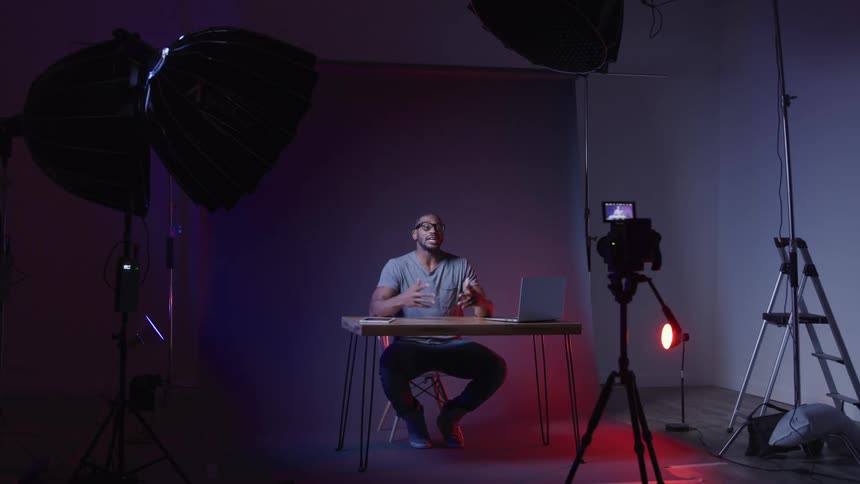 Man records himself while sitting at a table in a studio and talking