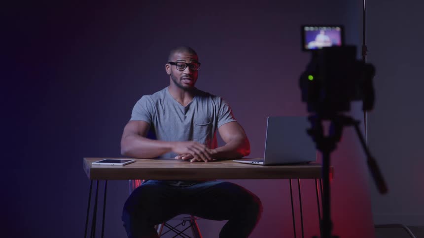 Cheerful man sitting at a table and recording a video facing a camera
