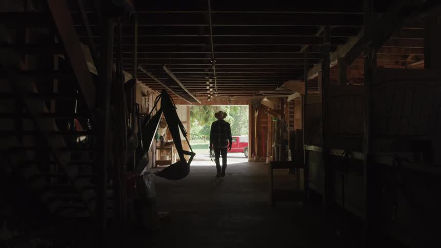 A cowboy carries a lasso through the stables