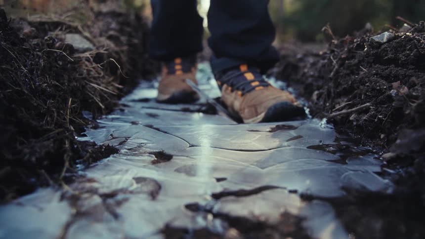 I person stomps on ice along a dirt trail