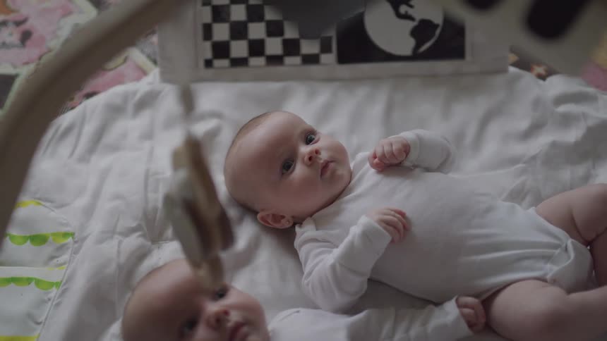 Two babies lying on a bed with one moving their limbs