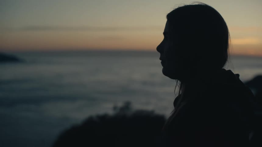 Silhouette of a person standing top of a mountain overlooking the ocean at sunset