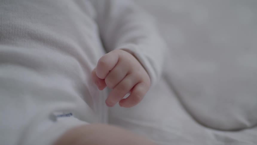 A baby lying on a bed and its tiny hand