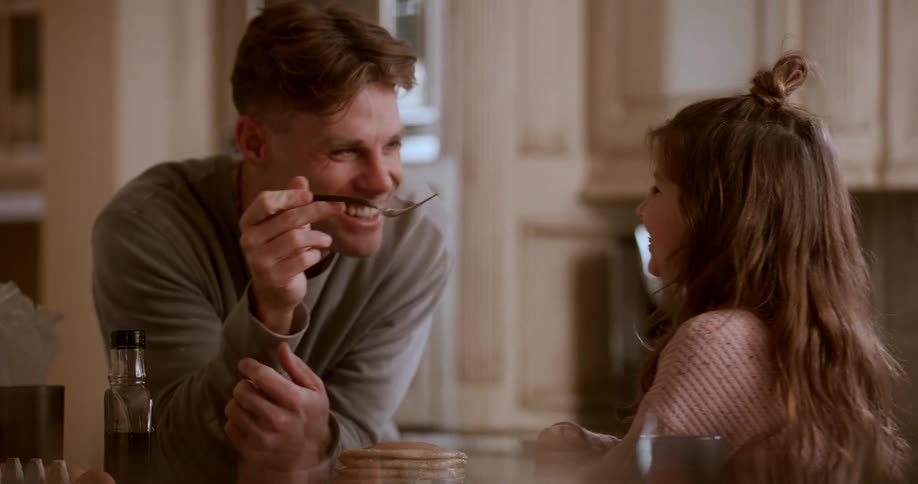 A brother is feeding pancakes to his younger sister using a fork