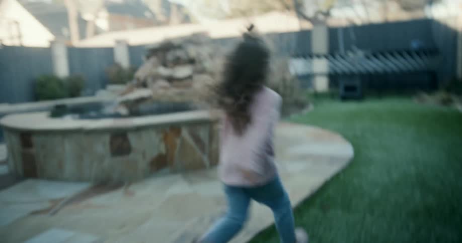A man running around and playing with his daughter in their backyard both laughing at midday