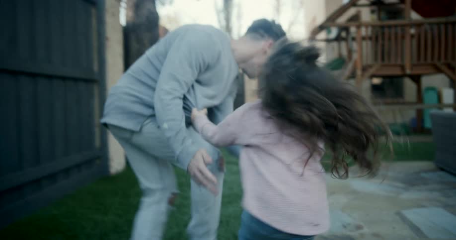 A father running around and playing happily with his daughter in their backyard playground