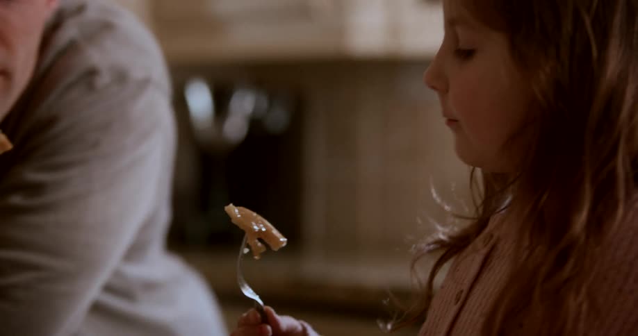 A man and a girl both picking up a piece of food with their cutlery towards their mouth