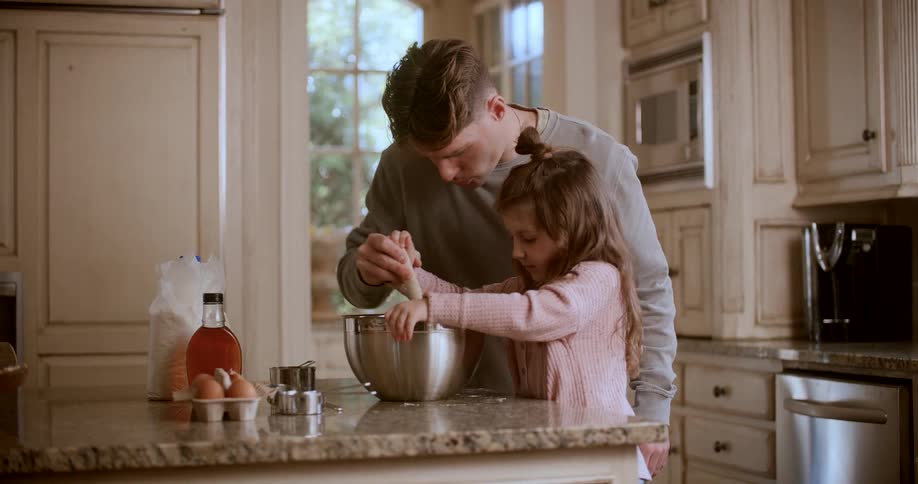 Man helps his daughter stir batter while they cook together in their kitchen