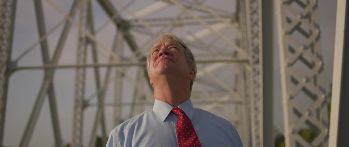 A man on a bridge looking up with sadness