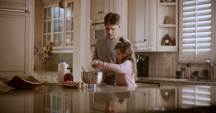 A girl pours flour into the bowl while her father watches