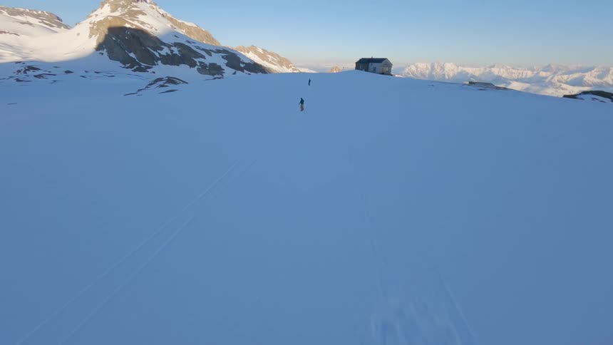 Aerial view of a snowy mountain and two people snowboarding at sunset