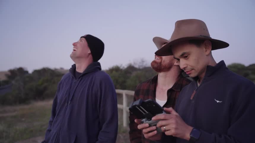 Three people looking up with one of them handling a remote control of a drone