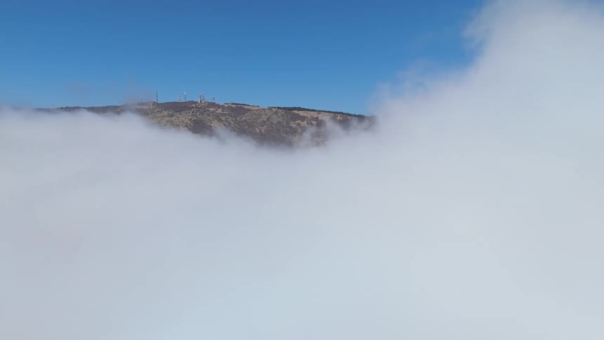 Low lying clouds passing below conceal all but the top of a mountain on a summer day