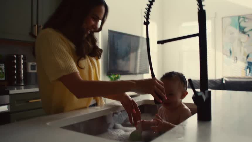 Mother having fun bathing her little son in the kitchen sink