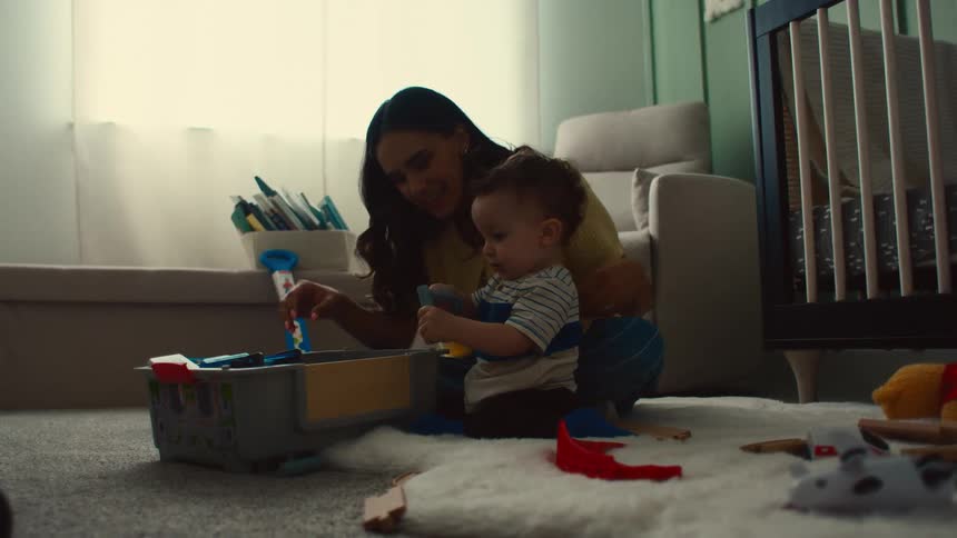 Mother sitting on a rug in a room playing with her little son