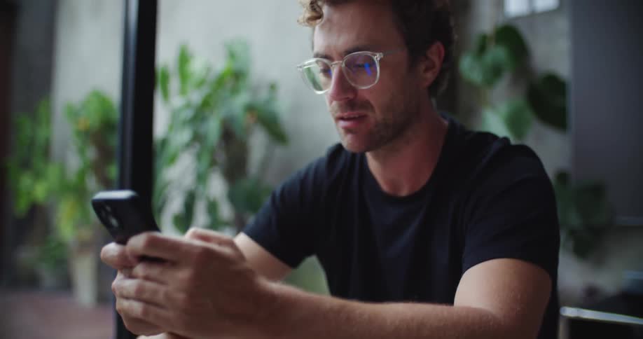 Man sitting in a room near a glass slider texting on his phone