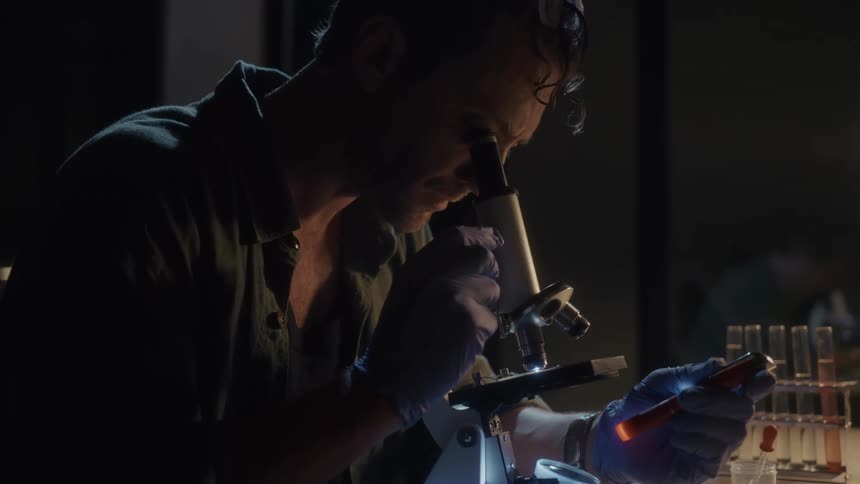 Man in a laboratory with a microscope analyzing a material